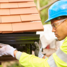 a young male roofer fixing plastic gutters
